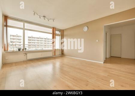 Radiateur et horloge montés sur les murs dans le spacieux salon vide de l'appartement moderne avec grande fenêtre et plancher de bois franc Banque D'Images