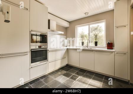 Plaque de cuisson à induction et évier au comptoir dans une cuisine spacieuse dans un appartement moderne avec fenêtre lumineuse et armoires blanches Banque D'Images