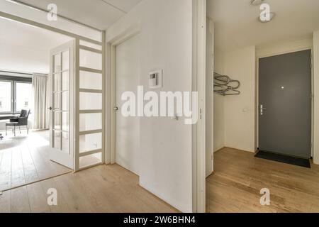 Une vue intérieure moderne et élégante mettant en valeur un espace lumineux avec des murs blancs, du parquet et des portes vitrées menant à une pièce meublée. Banque D'Images