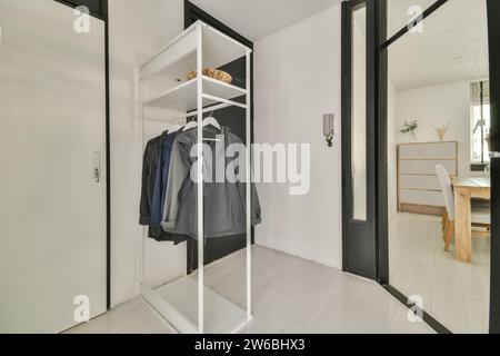 Une entrée élégante et moderne avec une armoire blanche ouverte avec manteaux, une vue sur une salle à manger baignée de lumière naturelle. Banque D'Images