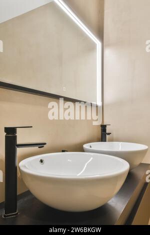 Une salle de bains moderne élégante avec deux lavabos blancs avec robinets noirs élégants, sous une lumière miroir LED géométrique. Banque D'Images