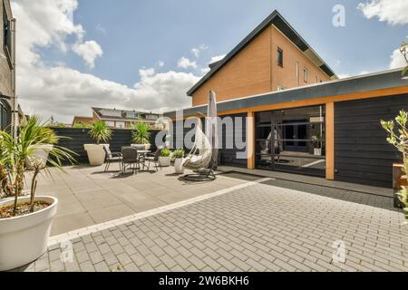 Patio contemporain avec mobilier d'extérieur élégant, plantes en pot et fauteuil balançoire élégant sous un ciel ensoleillé. Banque D'Images