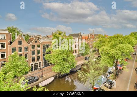 Vue panoramique sur le canal d'Amsterdam entouré d'arbres verdoyants et de bâtiments hollandais historiques sous un ciel bleu. Banque D'Images