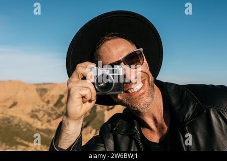 Un homme joyeux dans un chapeau prend une photo avec un appareil photo vintage sur fond panoramique Banque D'Images