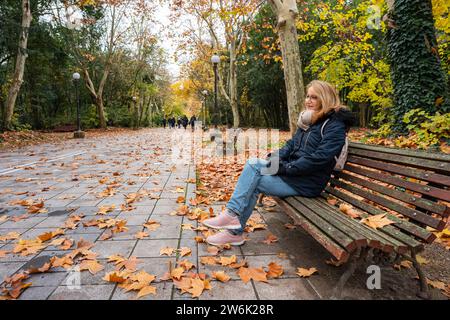 Femme assise sur un banc en bois dans un parc public par une froide journée d'hiver. Banque D'Images