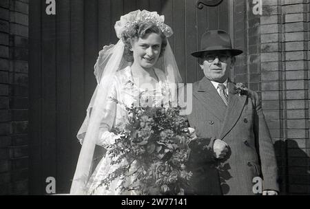 Années 1950, historique, mariage, une mariée debout avec son père, portant un costume croisé et un chapeau, pour une photo à l'extérieur de l'entrée de l'église, Angleterre, Royaume-Uni. Banque D'Images