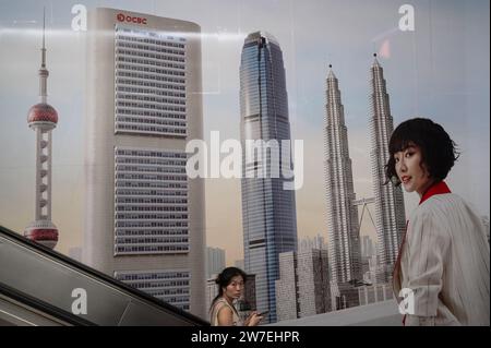 27.07.2023, Singapour, Singapour, Singapour, - Femme sur un escalator au centre d'affaires Raffles place devant un grand OCBC Oversea-Chinese Banking Corpor Banque D'Images