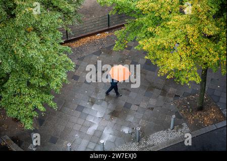 05.10.2023, Allemagne, Berlin, - Une personne avec un parapluie marche le long d'une rue humide dans le quartier Charlottenburg à Berlin un jour pluvieux d'automne. 0SL Banque D'Images