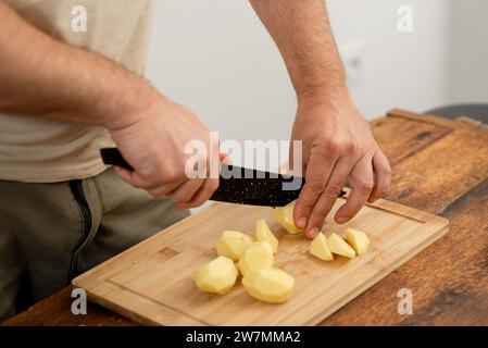 Cuire en tranchant les pommes de terre pelées pour la préparation du dîner sur une planche de bois. Banque D'Images