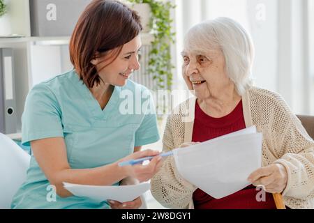 L'infirmière souriante donne des documents de femme âgée à lire dans le bureau du docteur Banque D'Images