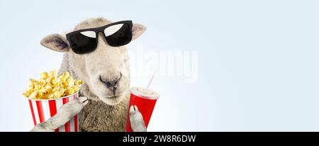 Drôle Hipster Sheep avec lunettes de soleil de mode tient Une coupe rouge de Cola et Un panier de Popcorn Rest et regarder un film sur Un fond bleu. Créatif I Banque D'Images