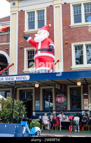 Père géant Noël devant le Harbour View Hotel à Millers point Sydney, décembre 2023, Nouvelle-Galles du Sud, Australie avec des gens mangeant et buvant Banque D'Images