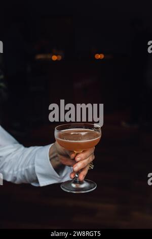 femmes plus âgées en chemise blanche à manches longues tenant cocktail gin pamplemousse brun orange dans un verre coupé avec fond sombre. espace de copie. Banque D'Images