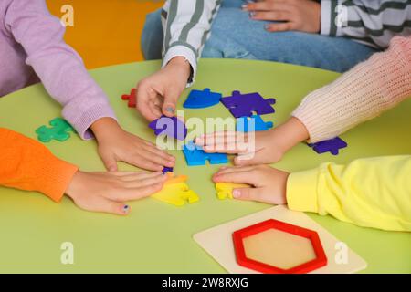 Petits enfants avec professeur de maternelle faisant puzzle à la table à la maternelle, closeup Banque D'Images