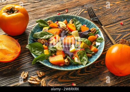 Assiette de salade délicieuse avec des graines de kaki, noix et grenade sur fond de bois Banque D'Images