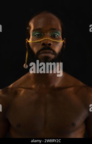 Homme gay afro-américain confiant barbu avec maquillage lumineux isolé sur fond noir, Close up portrait. Homme africain gay portant du maquillage regardant la caméra. Banque D'Images