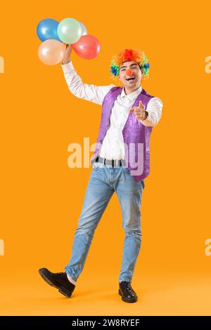 Heureux jeune homme en costume de clown avec des ballons sur fond jaune Banque D'Images