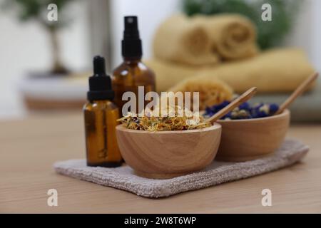 Bouteilles d'huiles essentielles, bols avec fleurs sèches et éponge naturelle sur table en bois clair, gros plan. Thérapie thermale Banque D'Images