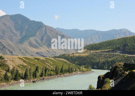 Un lit sinueux d'une large rivière à l'eau turquoise coulant dans un canal avec de hautes rives à travers une vallée de montagne pittoresque sur une journée ensoleillée d'été. K Banque D'Images