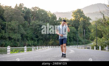 Un asiatique fatigué en vêtements de sport essuie sa sueur sur son visage tout en courant dehors. entraînement intense, épuisé Banque D'Images