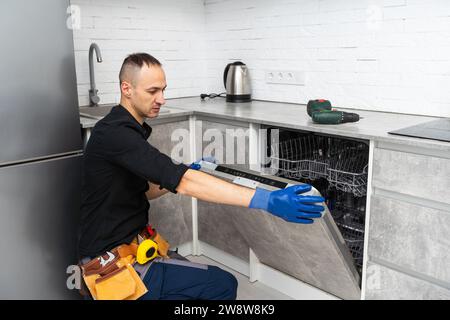 Young Repairman Fixing Dishwasher With Screwdriver In Kitchen Stock Photo