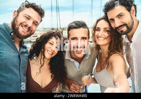 Un groupe d'amis joyeux prenant un selfie tout en grillant des verres dans une marina, incarnant la joie de l'amitié et de la célébration. Banque D'Images