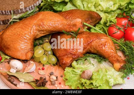 Quartiers de cuisse de poulet fumé avec herbes fraîches, tomates, tranches de pain et autres assaisonnements sur une planche à découper Banque D'Images