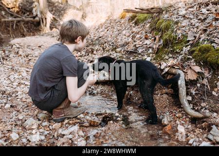 Jeune garçon et son chiot de compagnie jouant dans creek Banque D'Images