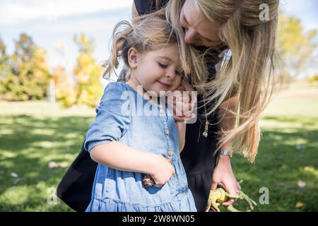 Maman embrassant sa fille souriante sur la tête et tenant sa main Banque D'Images