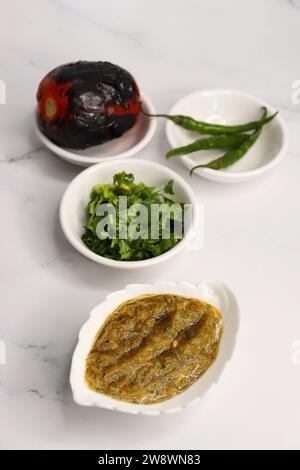 Sauce tomate rôtie maison ou chutney servi dans un petit plat en céramique sur fond blanc avec des ingrédients tomate rôtie, piment vert. Banque D'Images