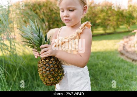 Petite fille mignonne porte un ananas dans ses mains Banque D'Images