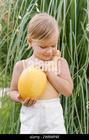 Petite fille mignonne tenant un melon jaune dans ses mains Banque D'Images