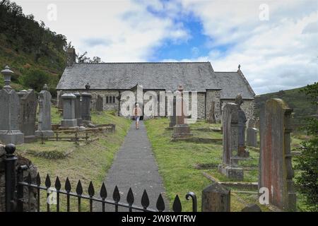 Femme marchant à travers le cimetière vers le porche d'entrée de St Davids Old Church, Llanwrtyd Wells, Powys, pays de Galles, Royaume-Uni Banque D'Images