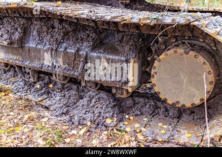 Gros plan d'une roue de crampon caterpillar sur un camion couvert de boue, terrain boueux sur le lieu de travail dans la construction de routes rurales dans une zone forestière Banque D'Images