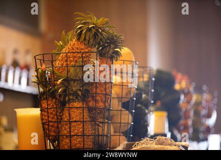 Une pile d'ananas mûrs est nichée dans un panier rustique en fil de fer sur une table en bois Banque D'Images