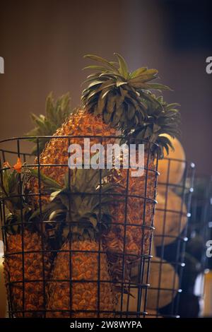 Une table en bois rustique affiche une nature morte vibrante d'ananas. Plusieurs ananas, certains entiers et d'autres tranchés, reposent dans un panier en fil de fer patiné Banque D'Images