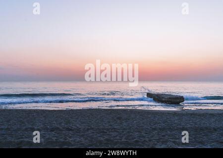 les vagues éclaboussent sur la roche au bord de la mer au coucher du soleil Banque D'Images