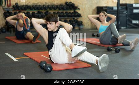 Homme athlétique faisant des exercices abdominaux pendant l'entraînement de groupe dans la salle de gym Banque D'Images