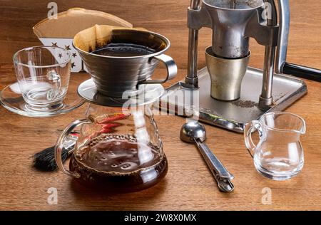 Vue à angle élevé de l'équipement pour égoutter le café, moulin à café, filtre en papier, porte-filtre, récipient en verre, cuillère et brosse sur la table en bois. Banque D'Images