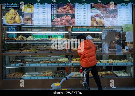 Une femme (peut-être une grand-mère) regarde devant un magasin d'alimentation avec son enfant dans les bras à Pékin, en Chine. 22-Dec-2023 Banque D'Images