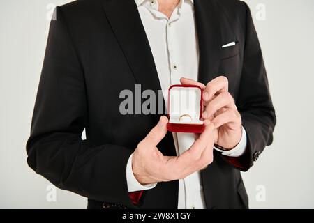 vue recadrée de l'homme en costume noir montrant boîte à bijoux avec bague sur gris, st valentines concept Banque D'Images