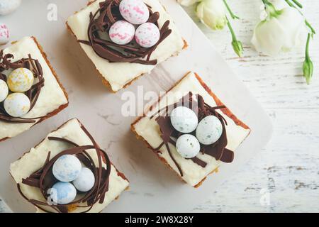 Barres de gâteau aux carottes de Pâques décorées avec nid de chocolat et œufs de bonbons au chocolat fleurissant des fleurs de cerise ou de pomme sur des fonds rustiques en bois clair. Banque D'Images