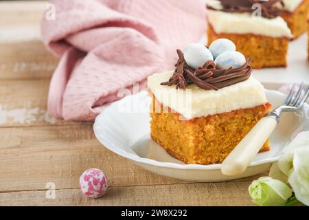 Barres de gâteau aux carottes de Pâques décorées avec nid de chocolat et œufs de bonbons au chocolat fleurissant des fleurs de cerise ou de pomme sur des fonds rustiques en bois clair. Banque D'Images