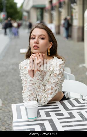 Portrait de la mode et jolie jeune femme en dentelle blanche haut assis près du café pour aller sur la table Banque D'Images