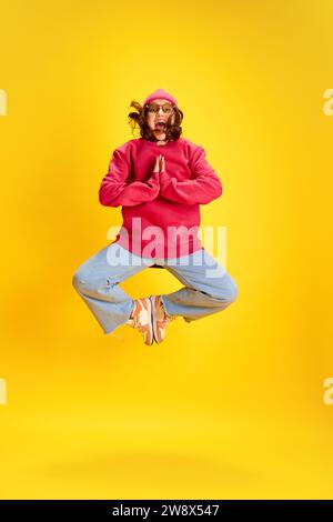 Portrait dynamique pleine longueur de folle, drôle jeune fille, adolescent posant dans l'air tout en sautant sur fond de studio jaune. Banque D'Images