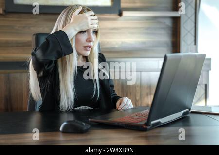 Femme d'affaires avec l'expression effrayée regarde l'écran d'ordinateur portable, serrant son front avec sa main dans la surprise Banque D'Images
