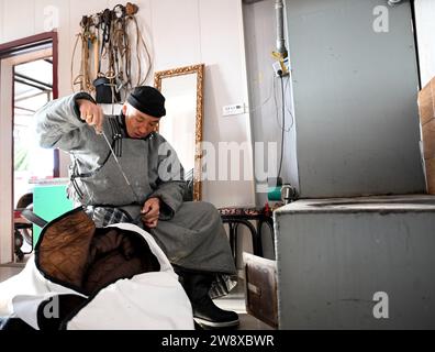 (231222) -- HULUN BUIR, 22 déc. 2023 (Xinhua) -- Erdendalai fabrique des vestes pour chevaux à la maison à Hulun Buir, dans la région autonome de Mongolie intérieure du nord de la Chine, 16 déc. 2023. L'hiver signifie généralement des défis pour les bergers vivant sur les prairies. Le froid intense et la neige affectent toujours leur vie quotidienne. Mais pour Erdendalai, un berger vivant à Hulun Buir, l'hiver est encore une saison chargée. En plus de prendre soin de plus de 200 têtes de bétail, moutons et chevaux qu'il possède, Erdendalai bénéficie également d'une activité importante de courses hippiques. Les chevaux ont toujours été un moyen de transport fiable et un in Banque D'Images