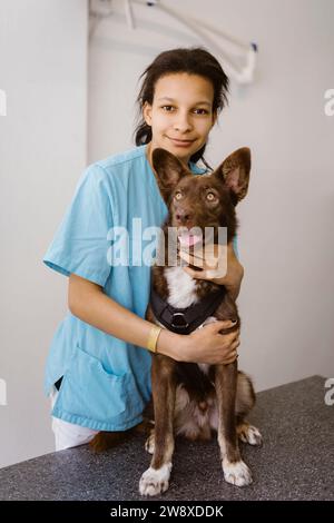 Portrait d'une infirmière embrassant un chien sur une table d'examen en clinique médicale Banque D'Images