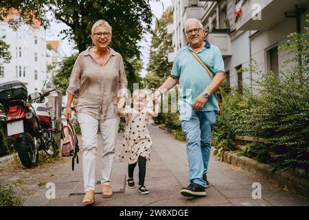 Heureux grands-parents tenant la main de la petite-fille tout en marchant dans la rue Banque D'Images