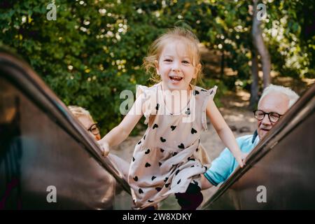 Portrait de fille souriante grimpant sur toboggan tout en jouant avec les grands-parents au parc Banque D'Images